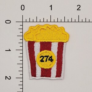 Peut inclure: Seau de popcorn &agrave; rayures rouges et blanches avec un cercle jaune contenant le num&eacute;ro 274. Le popcorn est jaune et a un bord festonn&eacute;.