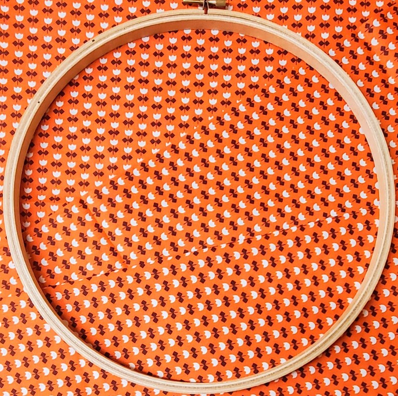 May include: A wooden embroidery hoop with a bright orange fabric background with a white pattern of small flowers. The hoop is empty and ready for embroidery.