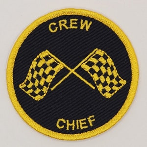 May include: A black and yellow embroidered patch with the words "CREW CHIEF" and two crossed checkered flags.