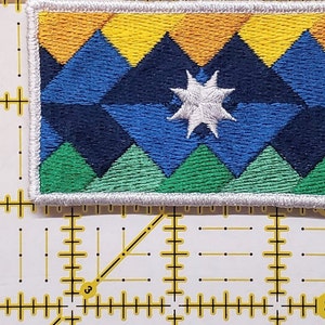 May include: A white embroidered patch featuring a blue, green and yellow mountain design. A white star is in the centre of the patch.