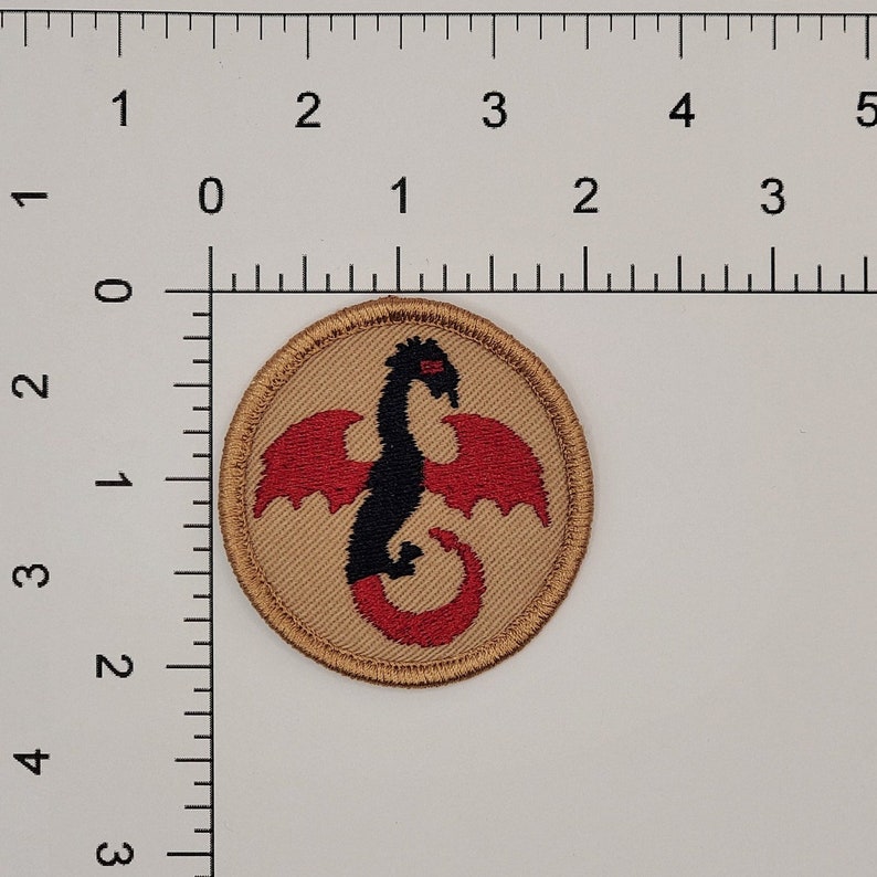 May include: A tan fabric patch with a gold border featuring a black dragon with red wings and tail.