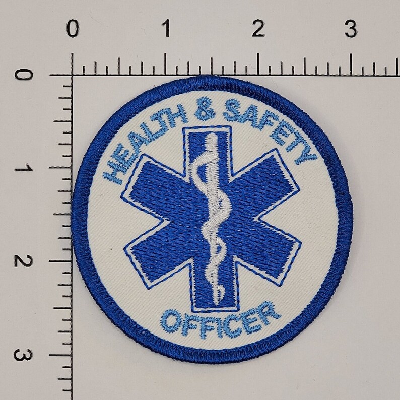 May include: A white embroidered patch with a blue star of life and the text "Health & Safety Officer" in a blue circle.