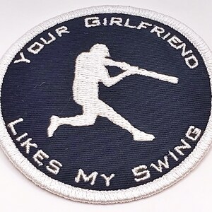 Op de afbeelding: Witte geborduurde patch op een donkerblauwe achtergrond met een honkballer die een knuppel zwaait. De tekst rond de rand luidt "Your Girlfriend Likes My Swing."