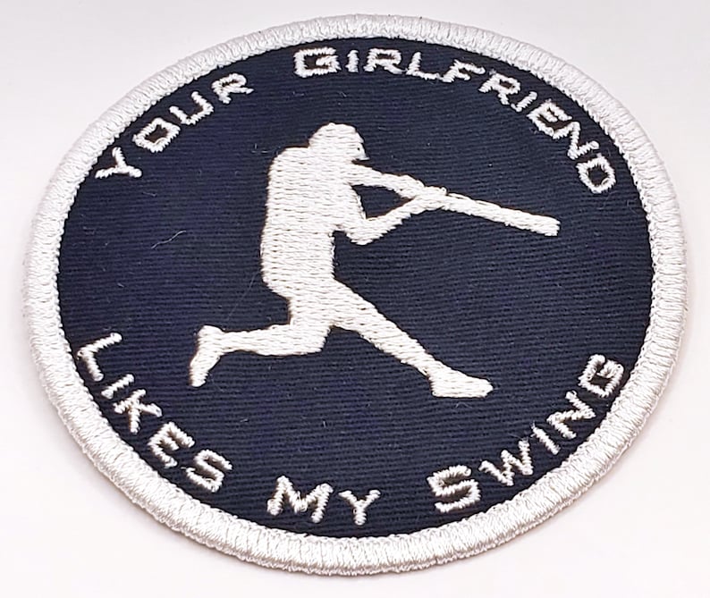 Op de afbeelding: Witte geborduurde patch op een donkerblauwe achtergrond met een honkballer die een knuppel zwaait. De tekst rond de rand luidt "Your Girlfriend Likes My Swing."