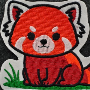 Pode incluir: Patch bordado com um panda vermelho de desenho animado. O patch tem uma borda branca e mostra o panda vermelho com p&ecirc;lo laranja e vermelho, olhos pretos e detalhes brancos. H&aacute; grama verde na parte inferior.
