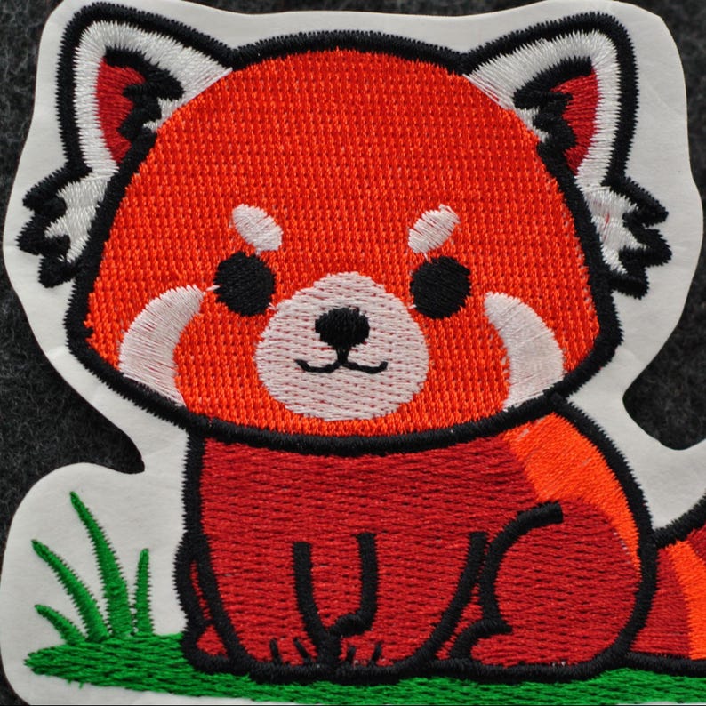 Pode incluir: Patch bordado com um panda vermelho de desenho animado. O patch tem uma borda branca e mostra o panda vermelho com p&ecirc;lo laranja e vermelho, olhos pretos e detalhes brancos. H&aacute; grama verde na parte inferior.
