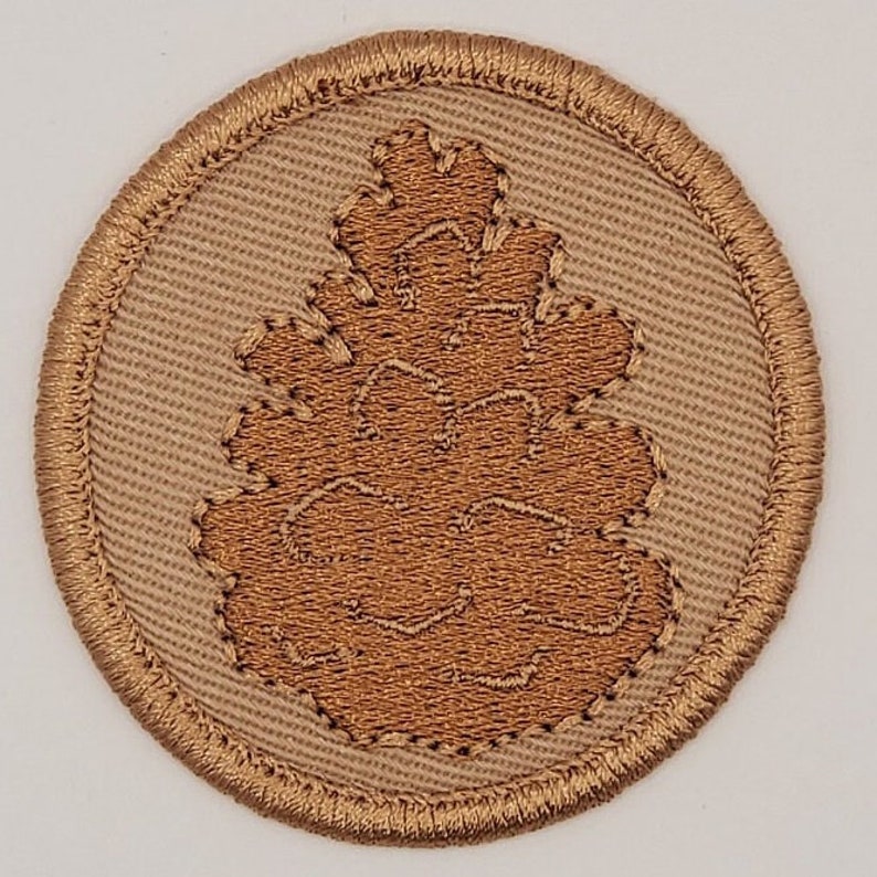 Puede incluir: Un parche bordado marr&oacute;n con un dise&ntilde;o de pi&ntilde;a marr&oacute;n sobre un fondo beige.