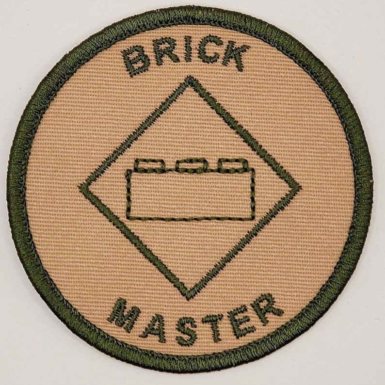 May include: A tan and green embroidered patch with the words "Brick Master" and a graphic of a Lego brick.