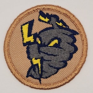 May include: Embroidered patch featuring a stylized gray and blue storm cloud with yellow lightning bolts. The patch has a tan background and a brown stitched border. The design is circular and suitable for jackets, bags, or other apparel.