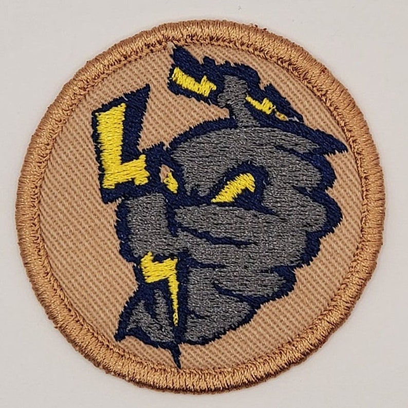 May include: Embroidered patch featuring a stylized gray and blue storm cloud with yellow lightning bolts. The patch has a tan background and a brown stitched border. The design is circular and suitable for jackets, bags, or other apparel.