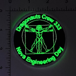 May include: A black and green embroidered patch with the text "Dragonaunts Crew 33" and "Nova Engineering Day" around a green outline of a Vitruvian Man.