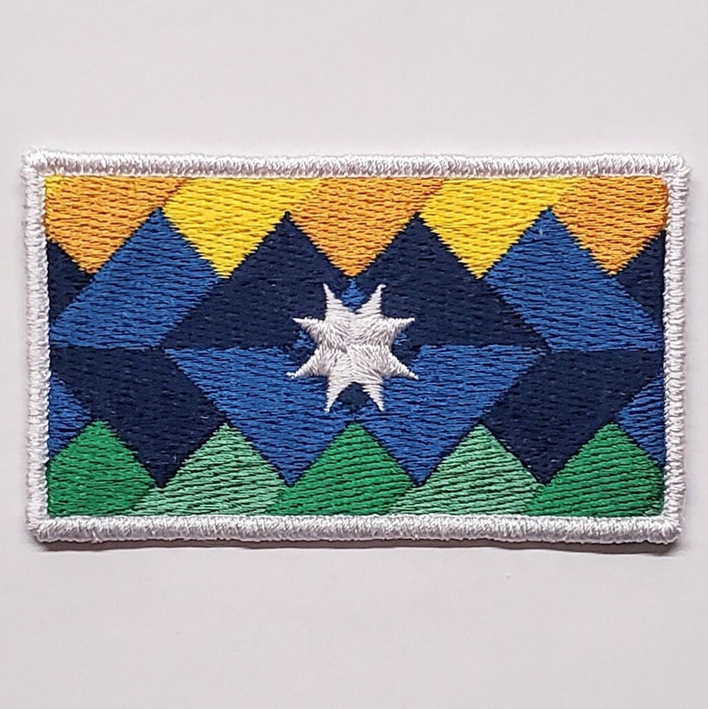 May include: An embroidered patch with a geometric design featuring a white star in the centre. The design is made up of yellow, orange, blue, green, and white triangles.
