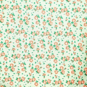 May include: A green fabric with a repeating pattern of small orange flowers. The flowers are scattered randomly across the fabric.