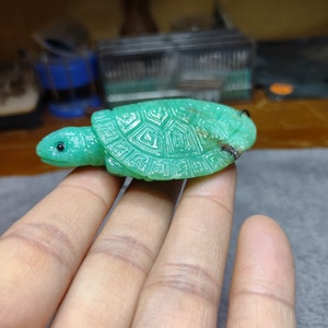 May include: A green jade turtle carving, with detailed shell markings, held in a hand.