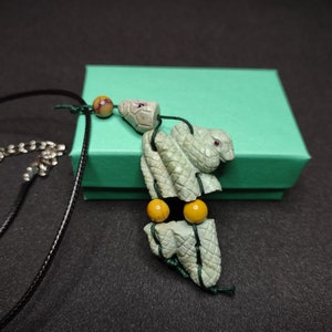 May include: A green jade necklace with a carved snake pendant and yellow beads. The necklace is on a black cord and comes in a teal gift box.