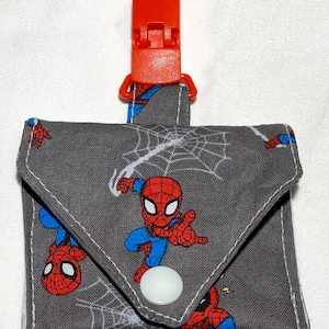 May include: A gray fabric pouch with a red plastic clip and a white button closure. The pouch features a repeating pattern of Spiderman characters and spiderwebs.