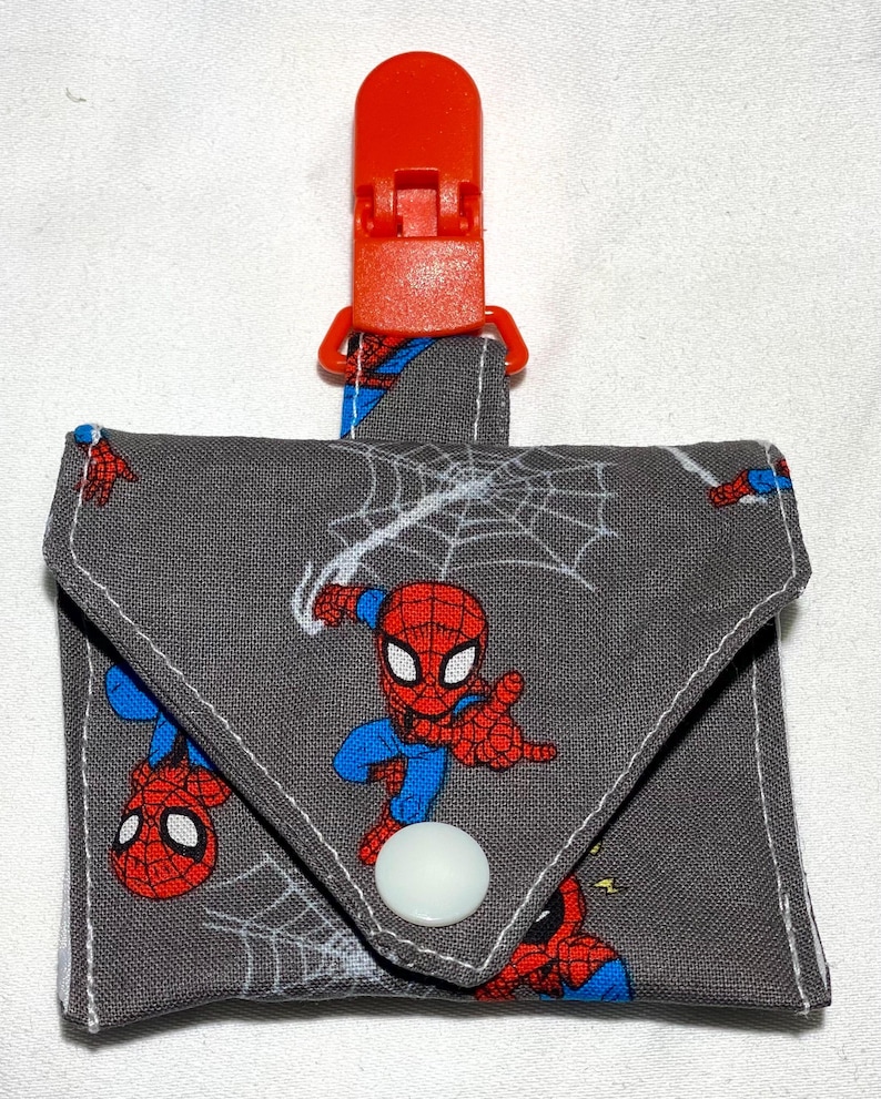 May include: A gray fabric pouch with a red plastic clip and a white button closure. The pouch features a repeating pattern of Spiderman characters and spiderwebs.