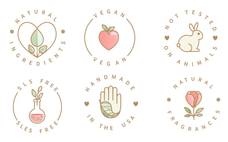 Puede incluir: Seis etiquetas circulares con contornos marrones y texto blanco. Las etiquetas presentan varios iconos y texto, incluyendo "Ingredientes naturales", "Vegano", "No probado en animales", "Libre de SLS", "Hecho a mano en los Estados Unidos" y "Fragancias naturales".