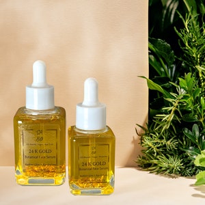 Puede incluir: Dos botellas de vidrio de suero facial bot&aacute;nico de oro de 24K. Las botellas son transparentes y contienen un l&iacute;quido amarillo con escamas doradas. Las botellas tienen tapas de gotero blancas y est&aacute;n etiquetadas con el nombre del producto y los ingredientes.