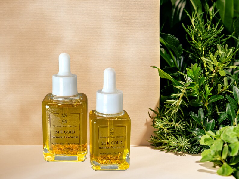 Puede incluir: Dos botellas de vidrio de suero facial bot&aacute;nico de oro de 24K. Las botellas son transparentes y contienen un l&iacute;quido amarillo con escamas doradas. Las botellas tienen tapas de gotero blancas y est&aacute;n etiquetadas con el nombre del producto y los ingredientes.