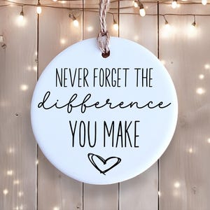 May include: White round bauble with black text that reads "Never forget the difference you make" and a small black heart.