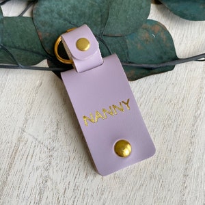 May include: A lavender leather keychain with a gold key ring and gold lettering that reads "NANNY".