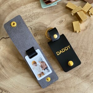 May include: A gray leather keychain with a photo insert and a black leather keychain with the word "DADDY" in gold lettering.