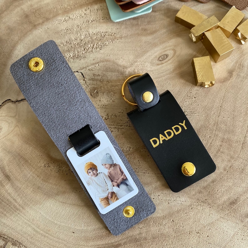 May include: A gray leather keychain with a photo insert and a black leather keychain with the word "DADDY" in gold lettering.