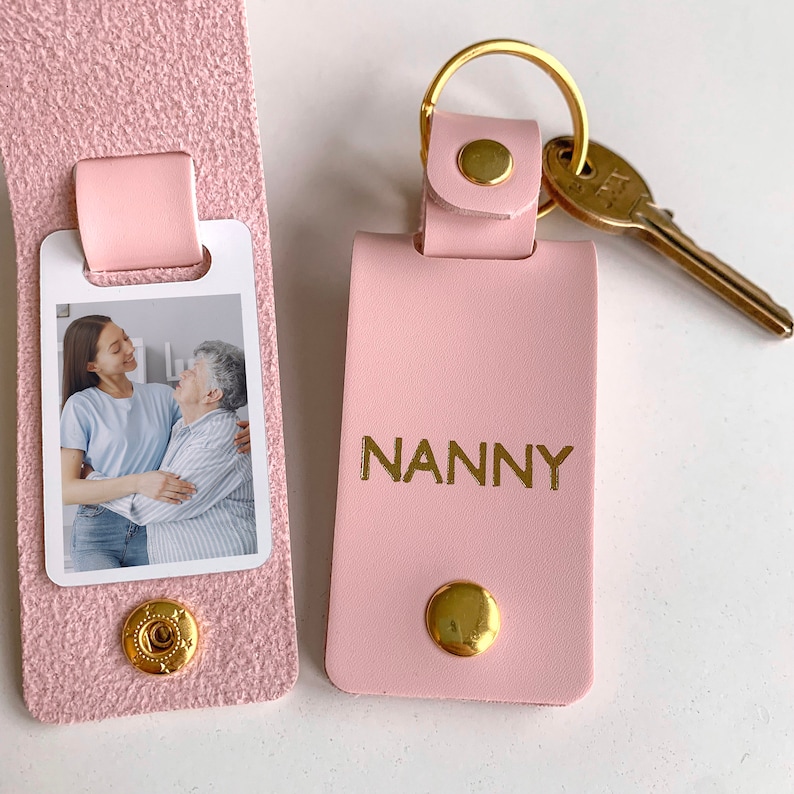 May include: Pink leather keychain with a gold key ring and a photo insert. The keychain has the word "NANNY" embossed in gold lettering.
