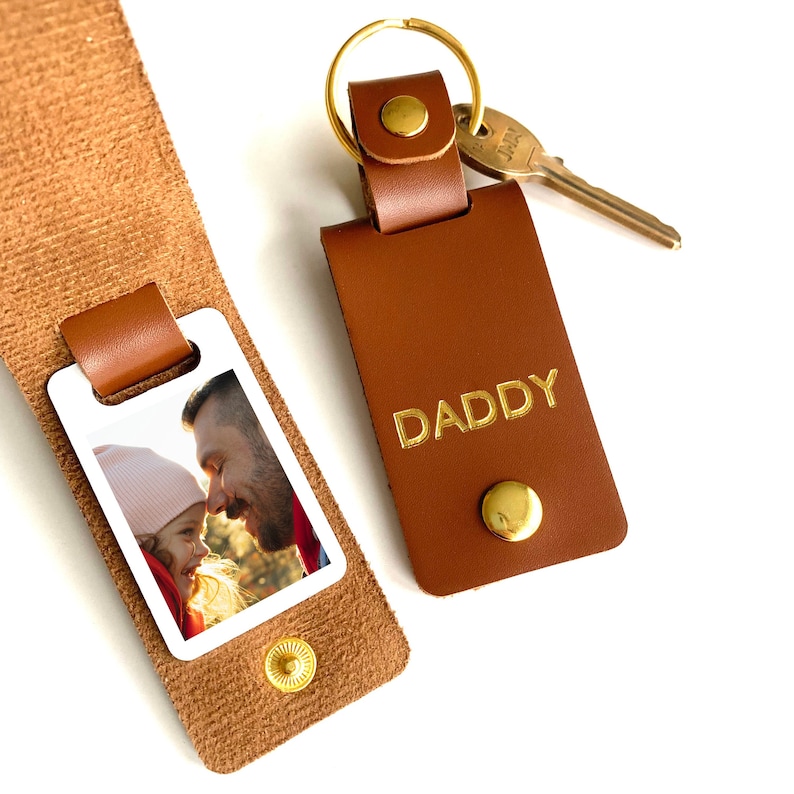 May include: A brown leather keychain with a photo insert and the word "DADDY" embossed in gold. The photo insert shows a father and daughter looking at each other.