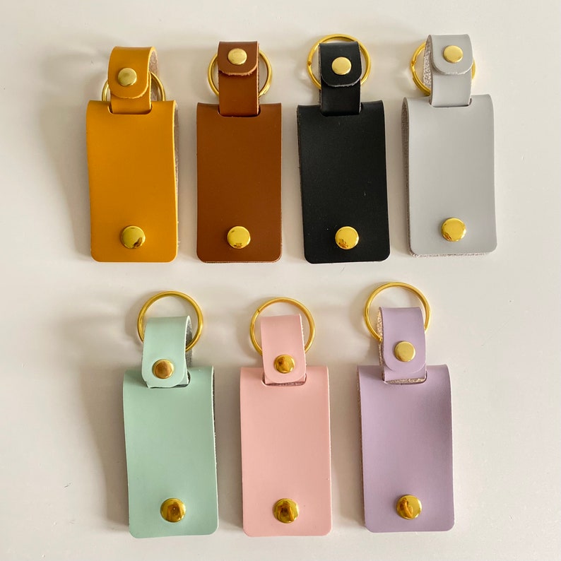 May include: Set of ten leather keychains with gold rings. The keychains are in various colors, including mustard yellow, brown, black, gray, light blue, pink, and purple.