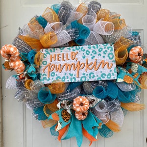 以下が含まれることがあります： 「Hello, Pumpkin」と書かれたサインが付いた、ターコイズブルー、白、オレンジの秋のリースです。