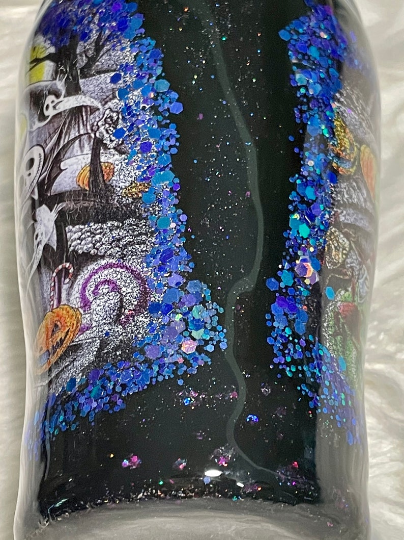 May include: A black tumbler with a glittery blue and purple design. The tumbler features a black and white image of a spooky Halloween scene.