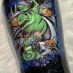 May include: A black tumbler with a glittery blue finish features a colourful illustration of characters from The Nightmare Before Christmas. The characters include Jack Skellington, Sally, and Oogie Boogie.