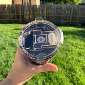 May include: A clear plastic lid with a black rubber seal and a small white button. The lid is on top of a black and purple tumbler.