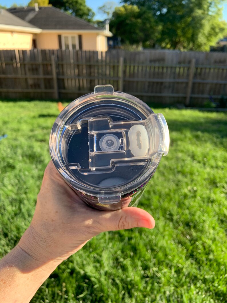 May include: A clear plastic lid with a black rubber seal and a small white button. The lid is on top of a black and purple tumbler.