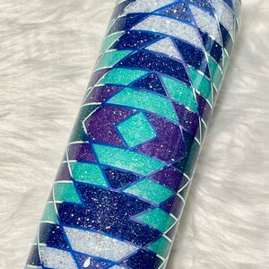 May include: A stainless steel tumbler with a geometric pattern in shades of blue, purple, and white. The pattern is made of glitter and has a shimmery finish.