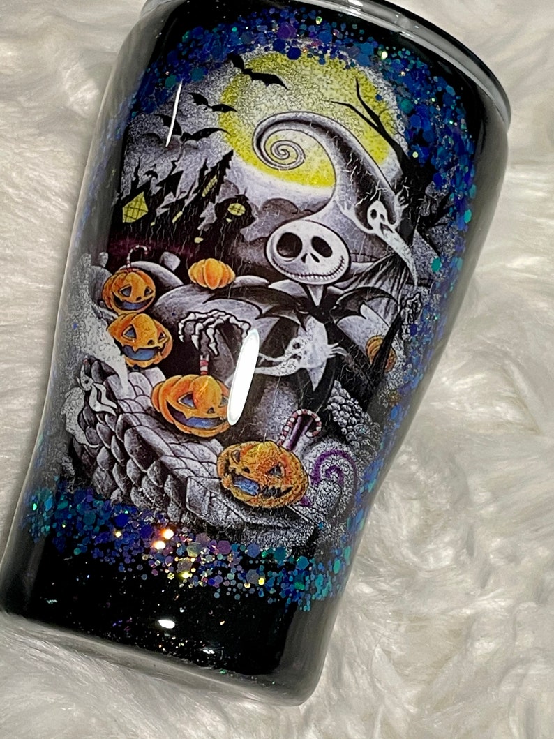 May include: Black and white tumbler with a glittery blue and black finish. The tumbler features a graphic of Jack Skellington from The Nightmare Before Christmas with pumpkins and bats.