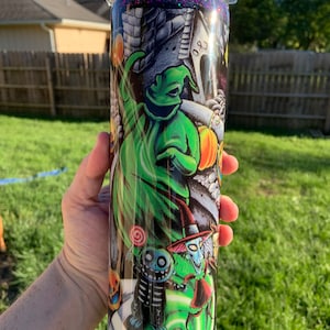 May include: A black and green tumbler with a glitter finish. The tumbler features a graphic of characters from the Nightmare Before Christmas, including Jack Skellington, Sally, and Oogie Boogie.