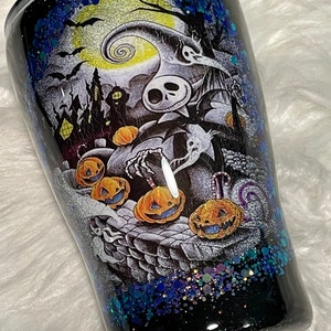 May include: A black and white tumbler with a glittery blue and purple finish. The tumbler features a graphic of Jack Skellington from The Nightmare Before Christmas with pumpkins and a spooky Halloween scene.