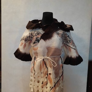 Peut inclure: Une veste en feutre blanche, marron et orange avec une ceinture à nouer. La veste a un design unique et abstrait et un col à volants.