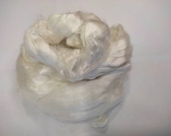May include: A close-up of a large clump of white silk fibres. The fibres are soft and fluffy, and they are arranged in a loose, irregular shape.