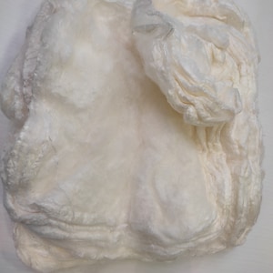 Peut inclure: Une sculpture blanche texturée de forme organique, réalisée en tissu superposé. La sculpture a une apparence douce et fluide, rappelant un nuage ou un morceau de bois flotté.