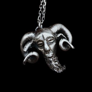 Op de afbeelding: Een zilveren ketting met een hanger met een gedetailleerd beeldhouwwerk van een geitenkop met hoorns en een baard.
