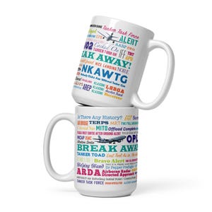 Może przedstawiać: Dwa białe ceramiczne kubki ułożone jeden na drugim. Górny kubek ma tekst o tematyce lotniczej i małą grafikę samolotu. Dolny kubek ma również tekst o tematyce lotniczej i grafikę samolotu. Kubki są białe z dużymi uchwytami.