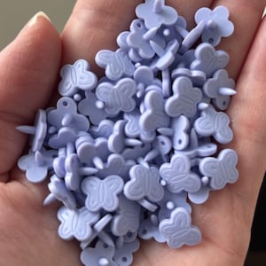 May include: A handful of light purple butterfly-shaped brads. Each brad features a butterfly design and a small, pointed post for insertion. These craft supplies are ideal for scrapbooking, card making, and other paper crafts.