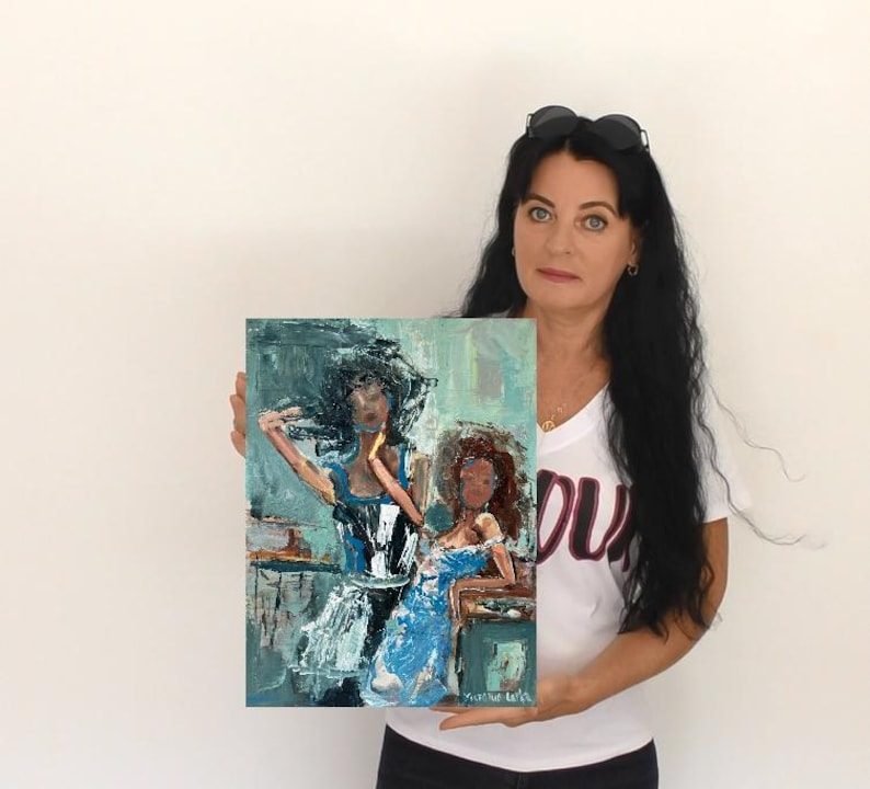 May include: An abstract painting featuring two women in blue dresses. The artwork has a textured, brushstroke style with a palette of blues, whites, and browns. The painting is held by a person in a white t-shirt.