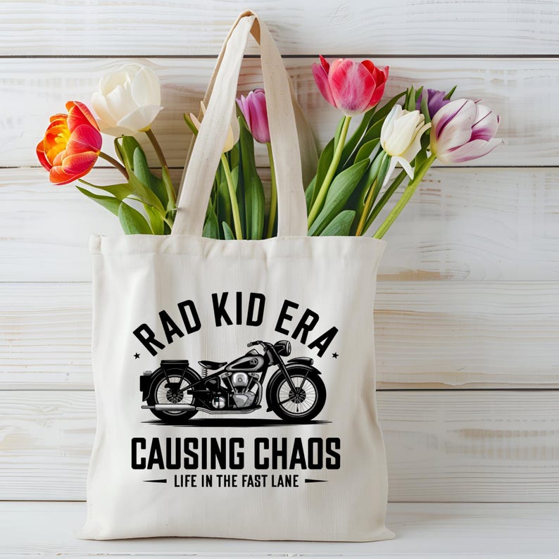 K&ouml;nnte beinhalten: Eine wei&szlig;e Canvas-Tragetasche mit schwarzem Text und einer Motorradgrafik. Der Text lautet "Rad Kid Era Causing Chaos - Life in the Fast Lane".