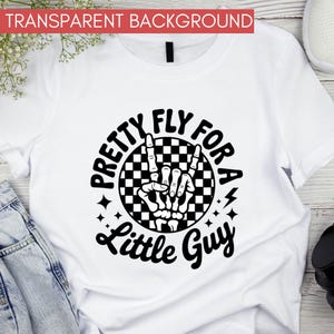 Puede incluir: Camiseta blanca con un gr&aacute;fico negro que dice "Pretty Fly For A Little Guy". El dise&ntilde;o presenta una mano de esqueleto haciendo el gesto de rock and roll, con un fondo a cuadros en blanco y negro.