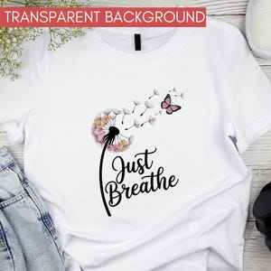 Może przedstawiać: Biała koszulka z motywem dmuchawca w r&oacute;żowych i brzoskwiniowych odcieniach, czarną łodygą i r&oacute;żowym motylem. Słowa "Just Breathe" są napisane kursywą pod dmuchawcem.